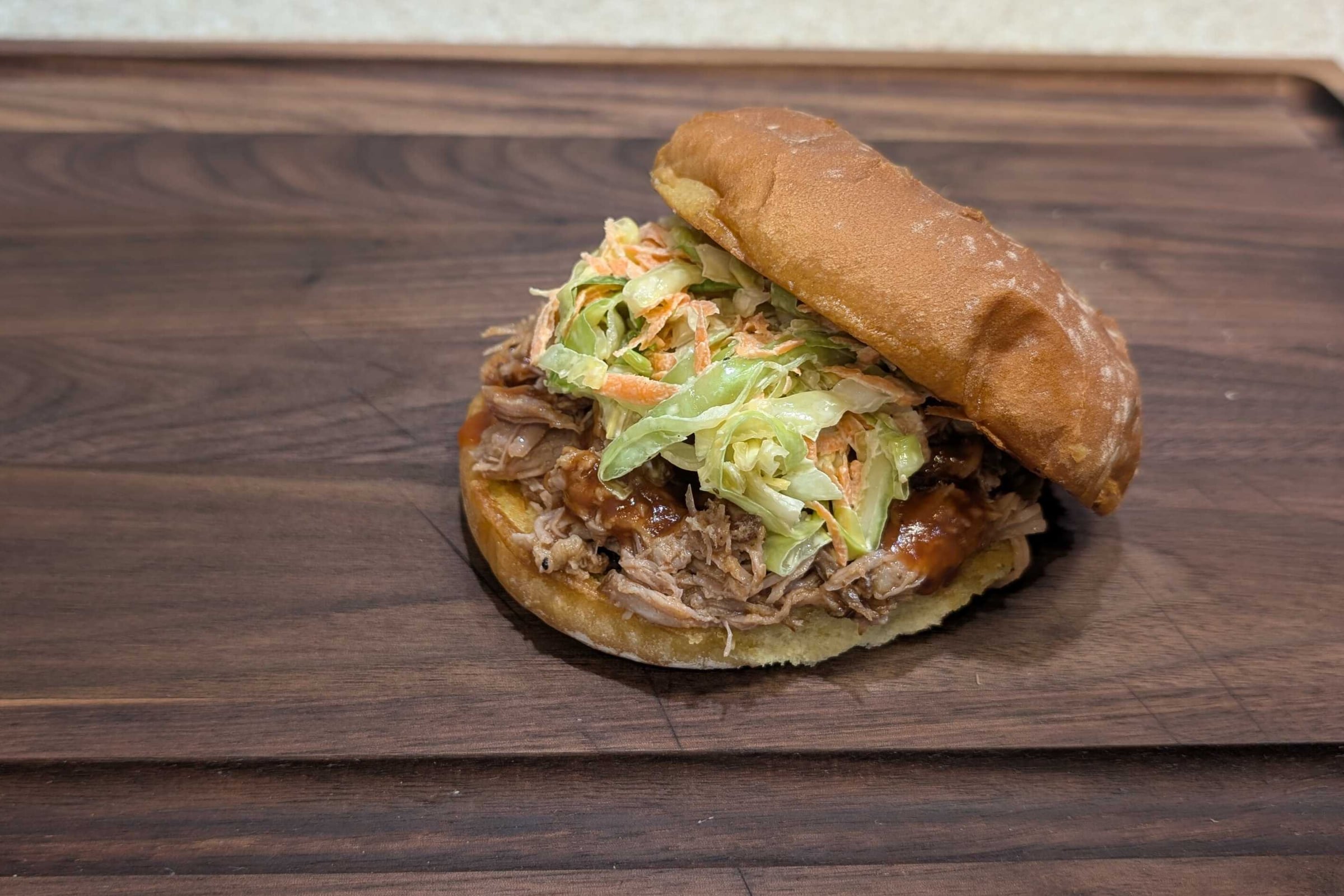 Pulled pork sandwich on a bun with sauced meat and coleslaw spilling out.